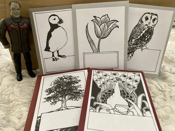 center White bookplates with illustrations - a puffin, a tulip, an owl, a tree, and a peacock, next to a Star Trek figurine.