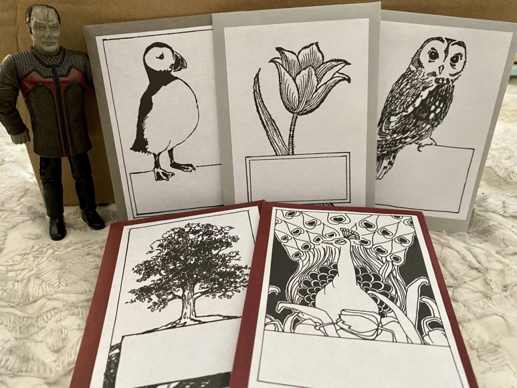 White bookplates with illustrations - a puffin, a tulip, an owl, a tree, and a peacock, next to a Star Trek figurine.